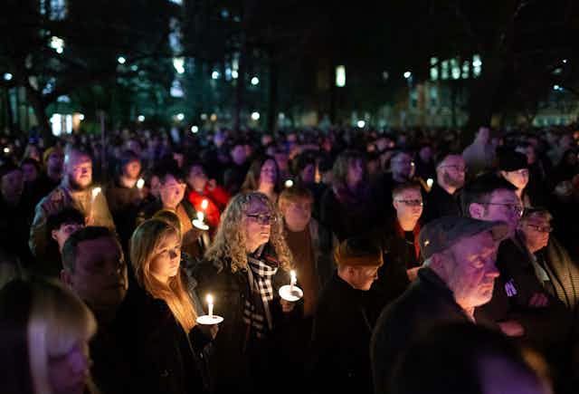 People gather at a vigil, holding candles. 