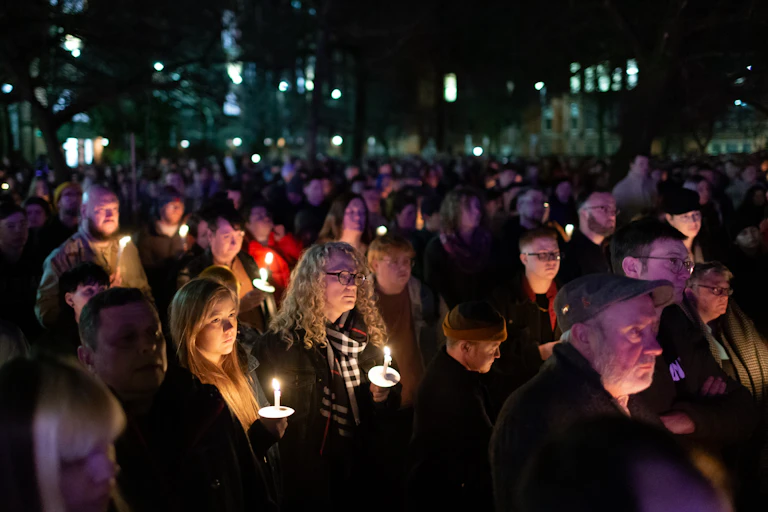 People gather at a vigil, holding candles.