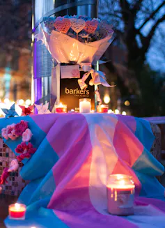 A trans pride flag is laid out with candles and flowers placed on top.