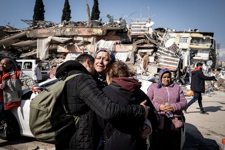 A group of people hug and cry amid rubble.