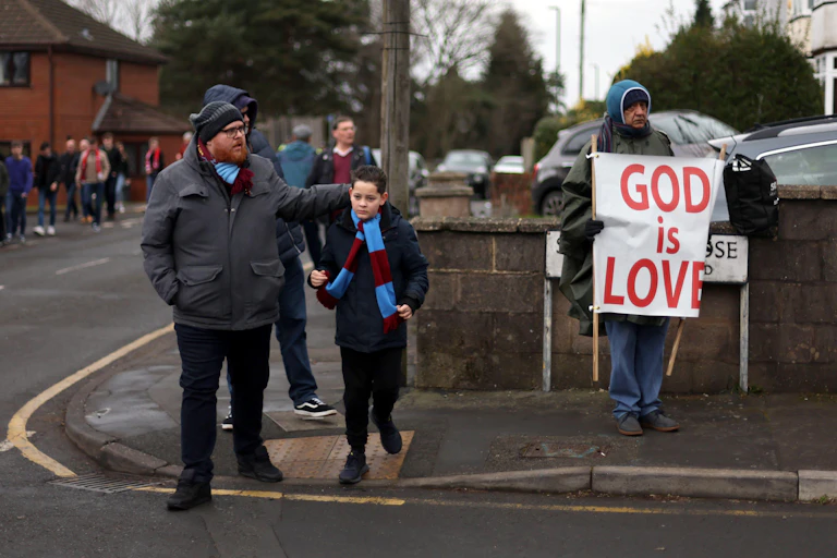 A father and son with football scarves next to a man holding a religious banner