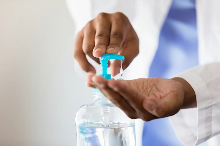 Person wearing white coat using hand sanitizer