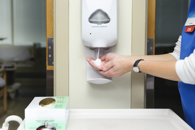 Nurse washing hands with foamy hand sanitizer from dispenser.