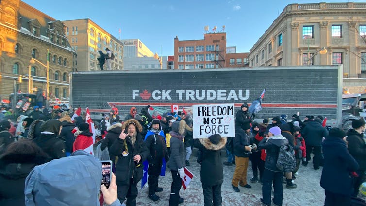 a group of people holding a sign reading FREEDOM NOT FORCE stand in front of a truck with FUCK TRUDEAU printed on the side