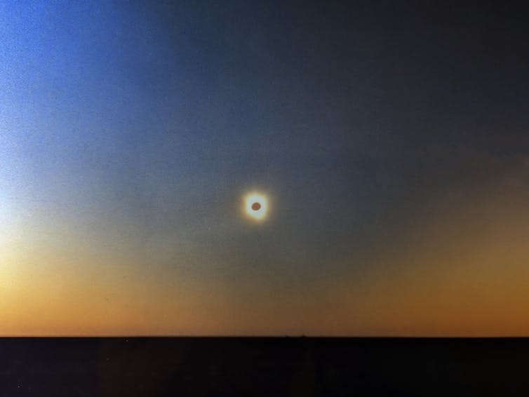 The dark spot of the eclipsed Sun is surrounded by a broad ring of white light, the corona