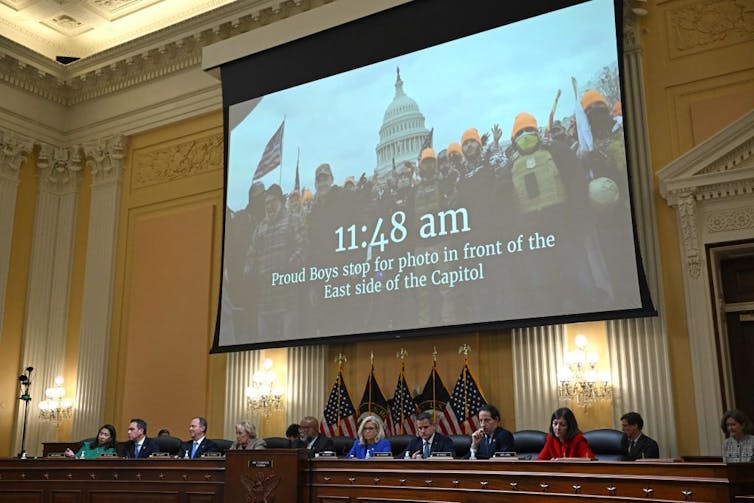 A huge screen shows an image of men in orange hats in front of the U.S. Capitol.