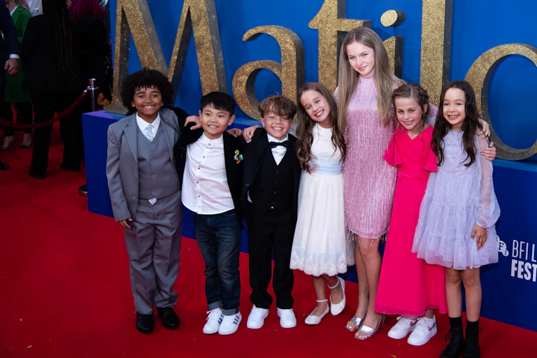 Children seen smiling around an older figure in front of the words 'Matilda'