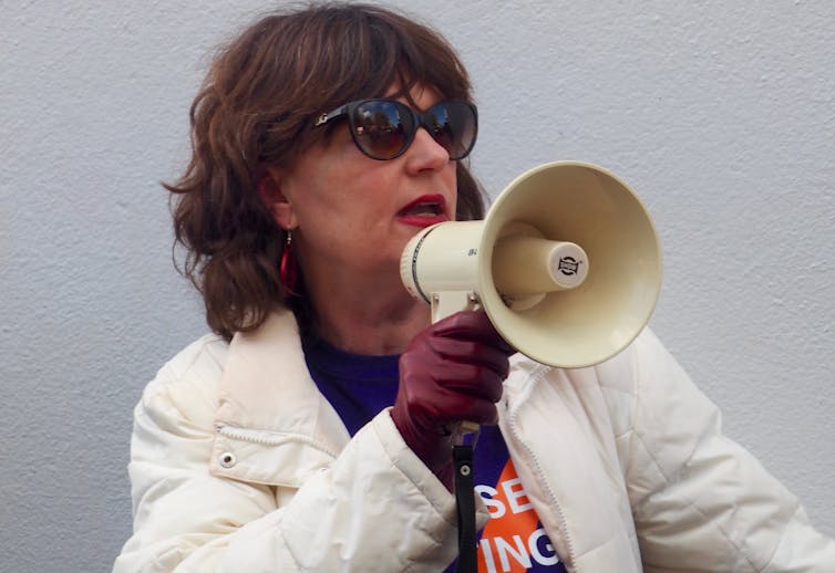 A woman wearing sunglasses and speaking into a megaphone