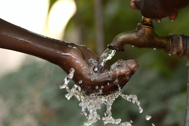 A person's hand is pictured turning on a brass tap while their other hand scoops up the water flowing from it