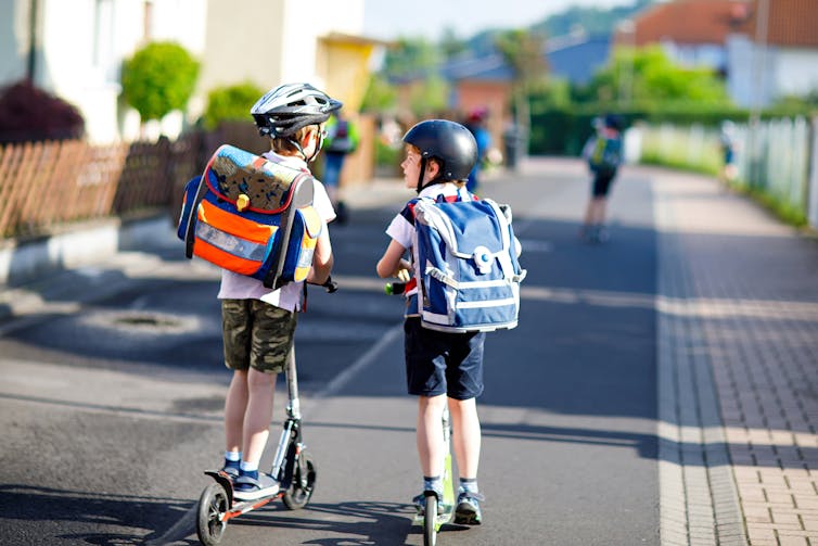 Dos niños de espaldas con mochila casco y patinete por un carril segregado.