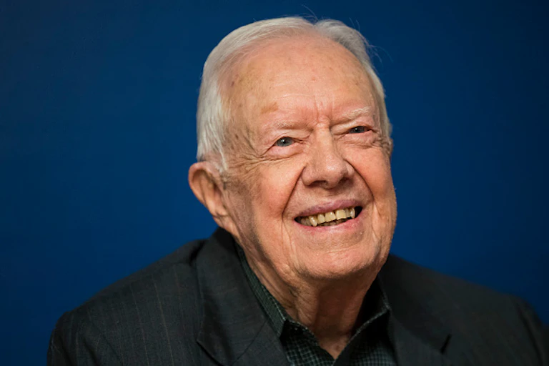 An old man with thinning hair smiles heartily.