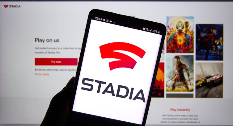 A phone shows the Stadia loading screen, in front of a computer screen with the website log in page.