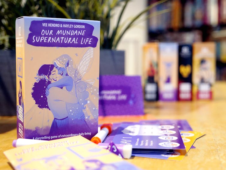 A box copy of Our Mundane Supernatural Life standing behind a series of cards and markers.
