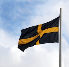 A black flag with a yellow cross flies with a blue sky in the background.