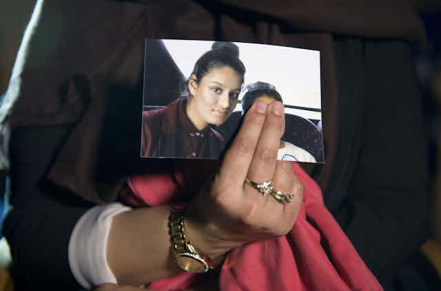 A woman's hand holds a photograph of a young Shamima Begum, taken before she left for Syria. The woman holding the photo is covering the face of another person in the photo with Shamima.