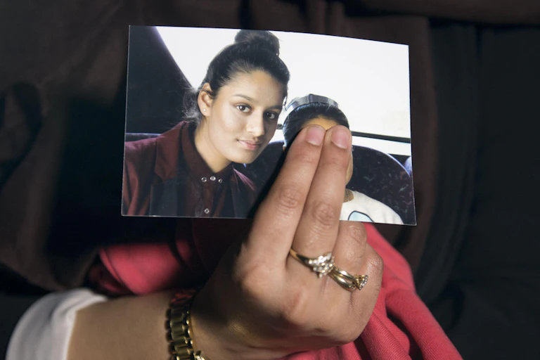 A woman's hand holds a photograph of a young Shamima Begum, taken before she left for Syria. The woman holding the photo is covering the face of another person in the photo with Shamima.