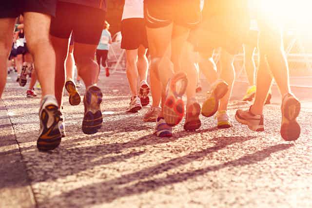 Piernas y pies de varios corredores de maratón vistos de espaldas contra el sol.