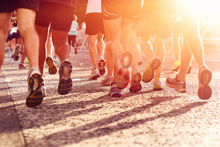 Piernas y pies de varios corredores de maratón vistos de espaldas contra el sol.