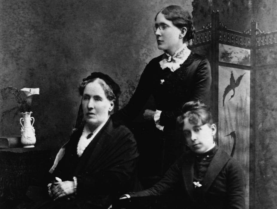 A black and white photograph showing three women, two of whom are seated.