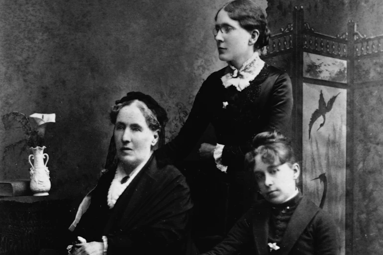 A black and white photograph showing three women, two of whom are seated.