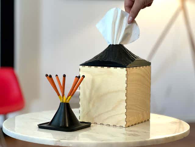 A hand removes a tissue from a volcano-shaped tissue box.