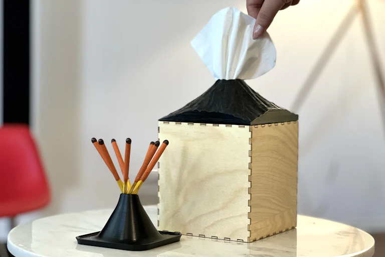 A hand removes a tissue from a volcano-shaped tissue box.