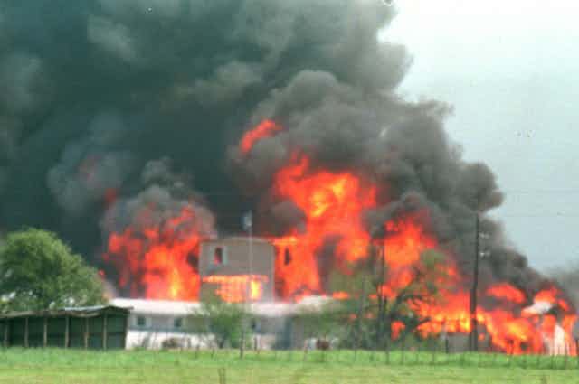 A tan building burns, with huge billows of smoke and fire coming out of it.