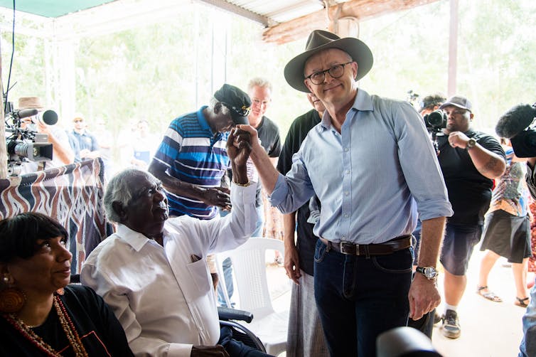 man in hat holds up hand of seated man