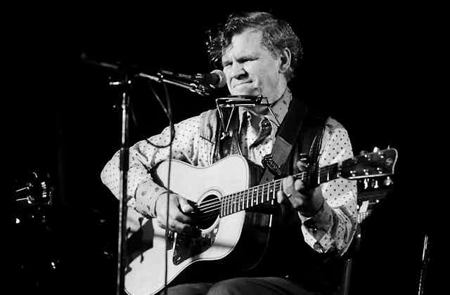 a black-and-white photo of a seated man playing an acoustic guitar