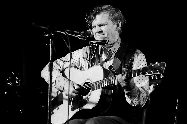 a black-and-white photo of a seated man playing an acoustic guitar