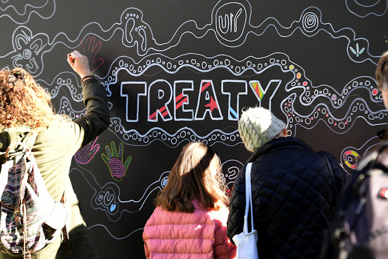Blackboard with "treaty" written on it and people adding decorations and hand prints in chalk.