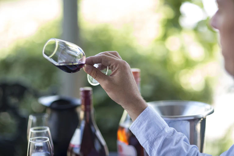 A man holding a glass of wine tilted at an almost 90 degree angle.