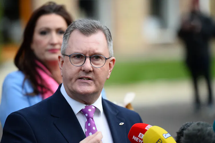 Jeffrey Donaldson speaking into a press microphone outdoors.