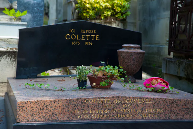 The black gravestone of Colette with some flowers and plants and an empty urn.
