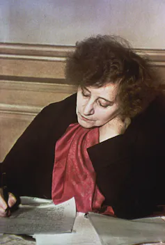 Coletter as an older woman, writing at her desk.