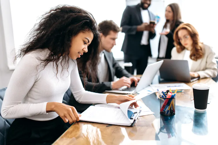 Woman doing paperwork in modern office, co-workers in the background.