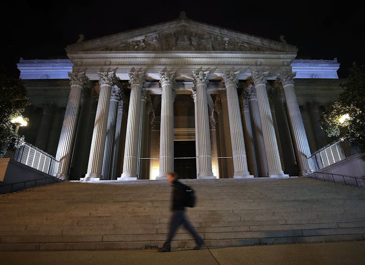 A large building at the top of wide stairs that has a facade featuring many columns.