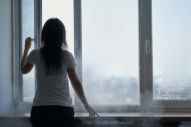 Mujer de espaldas abriendo una ventana empañada por el frío.