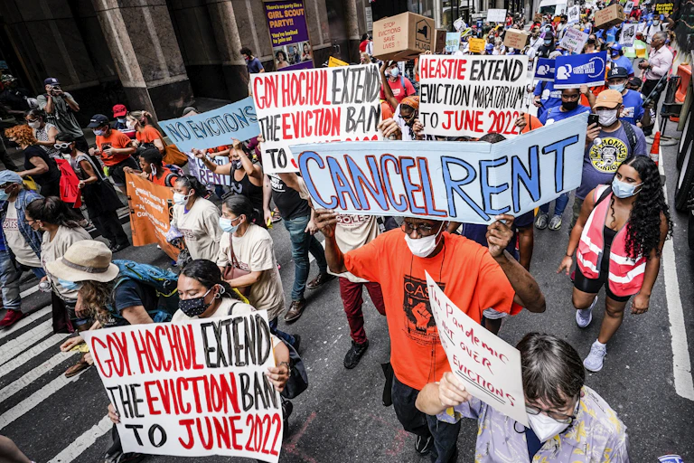 lots of people carrying signs like cancel rent march through a street