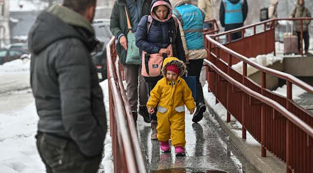 People who are bundled up walk in wintry weather along an outdoor ramp.