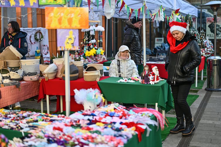 Women work at and browse an outdoor Christmas market.