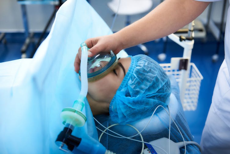 Person under anesthesia during surgery, gas mask over face
