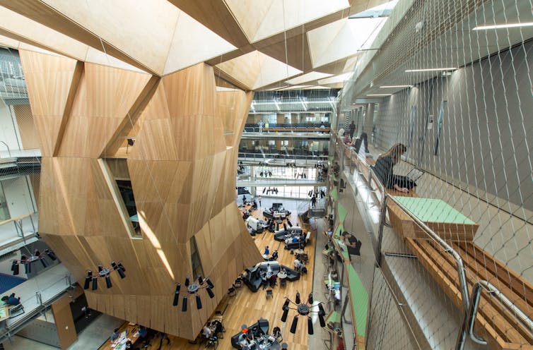 Interior of Melbourne School of Design at Melbourne University, a woman sits on a bench with a laptop