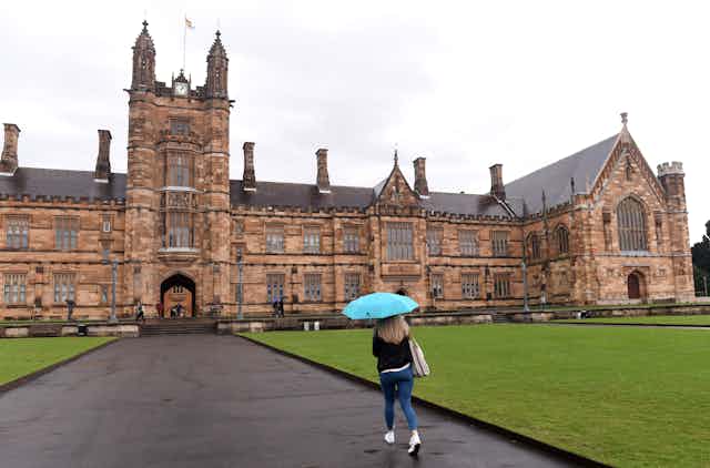 Woman with umbrella, approaching the main sandstone building at Sydney University. 