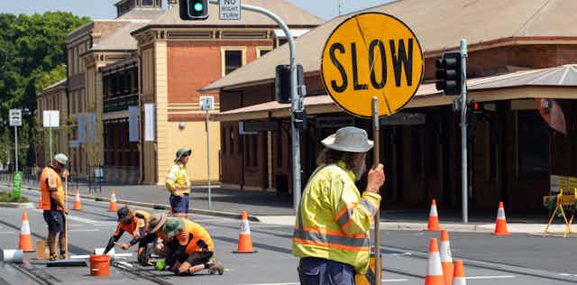 Road worker holds stop sign while colleagues work on tram tracks