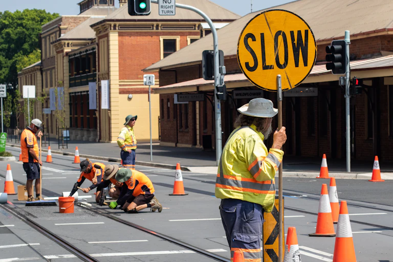 Road worker holds stop sign while colleagues work on tram tracks
