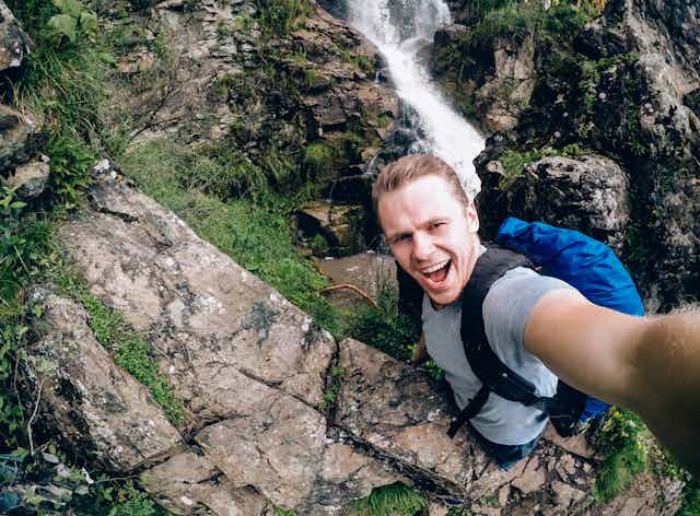Man standing at edge of cliff or waterfall taking selfie