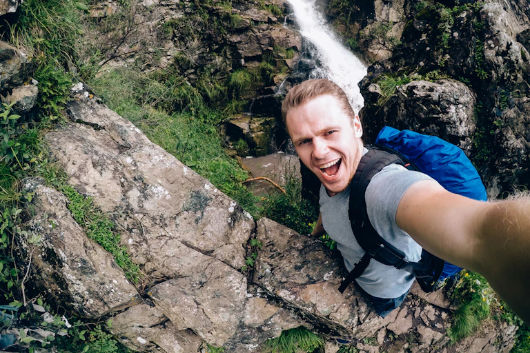 Man standing at edge of cliff or waterfall taking selfie
