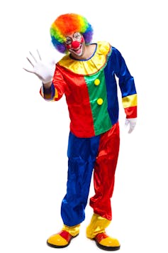 A man in a red, blue, green and yellow clown suit waves at us. He has a multicoloured wig, white makeup and a big red nose.