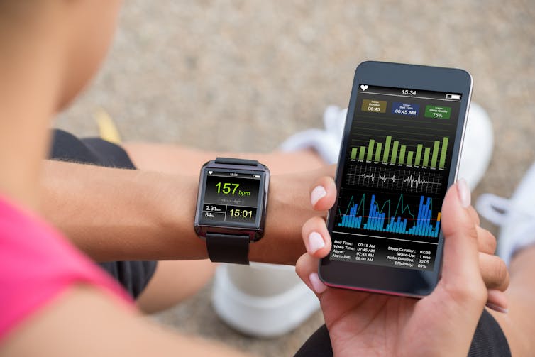 Female runner looking at her mobile and smart watch heart rate monitor.